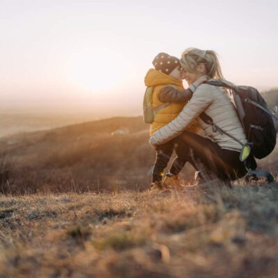 Mom hugging toddler on a hiking trail with the sunset in the background.