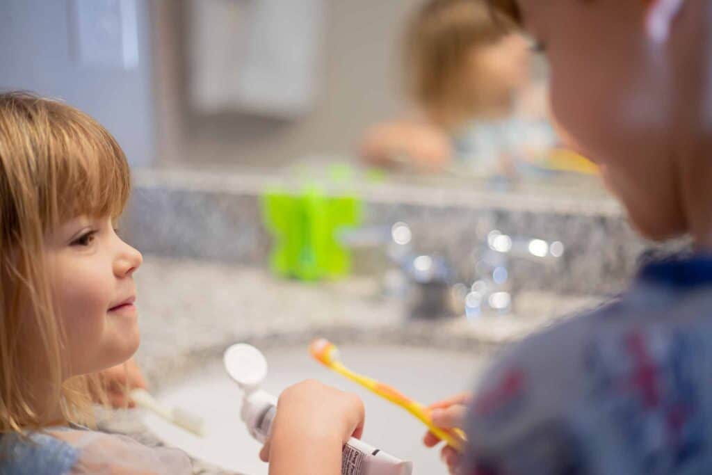 Brother and sister brushing teeth together, smiling. 