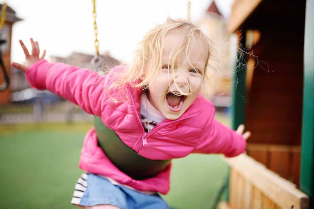 Excited girl on a swing at a playground. 