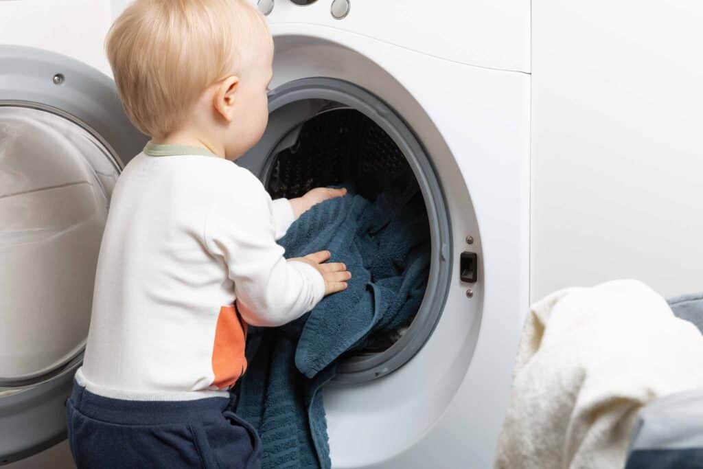 Image of a toddler boy doing chores, loading the washing machine. 
