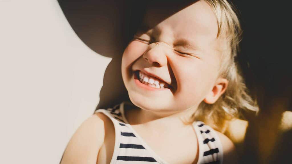 Cutest little girl smiling and squinting in sunlight. 
