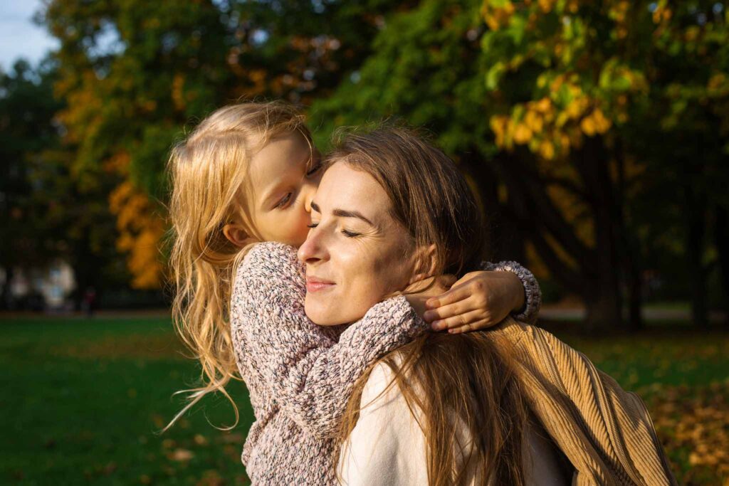 Young woman and child girl joyfully hugging in the park.